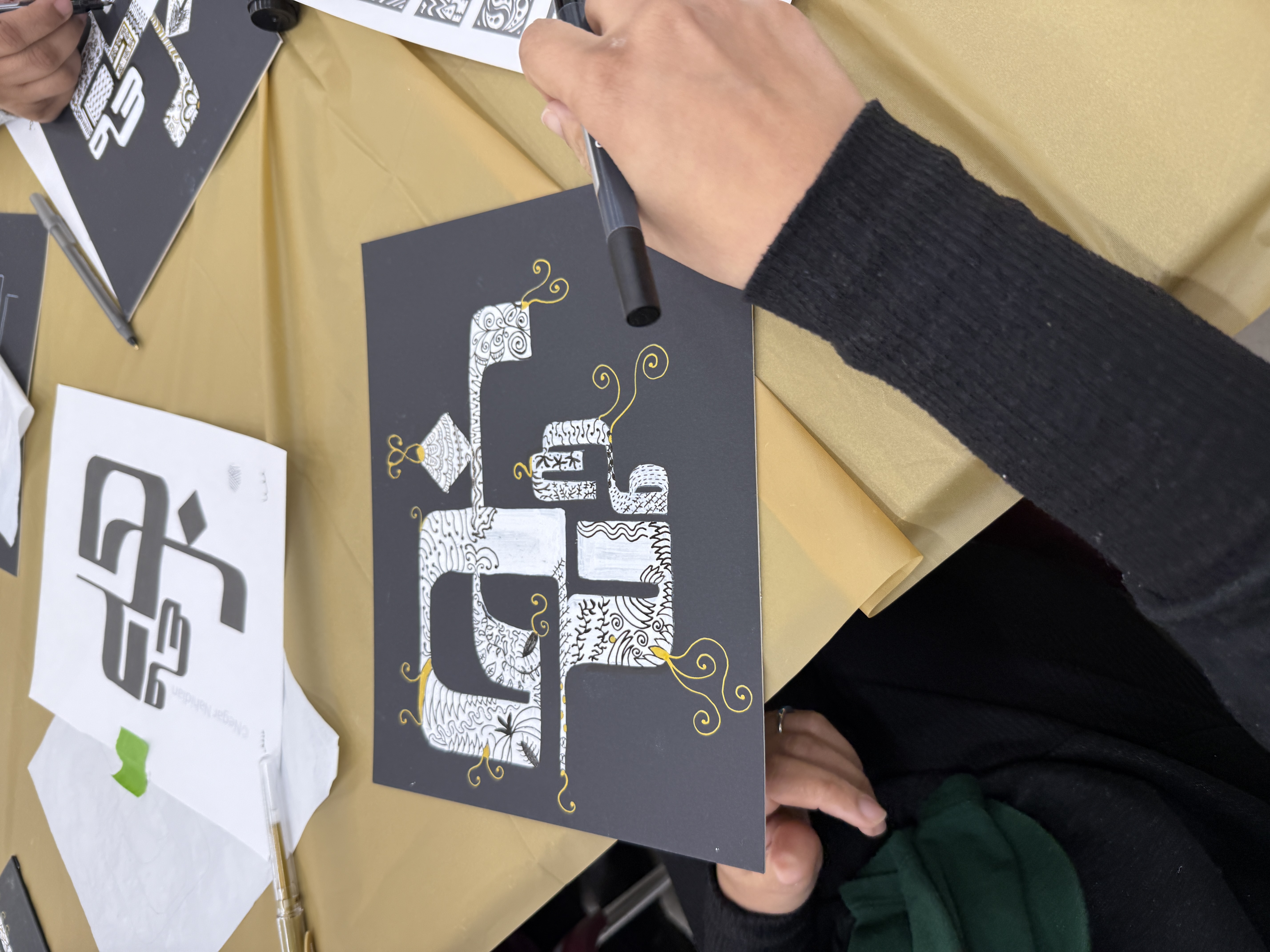 Participant adding gold detail to a patterned calligraphy piece