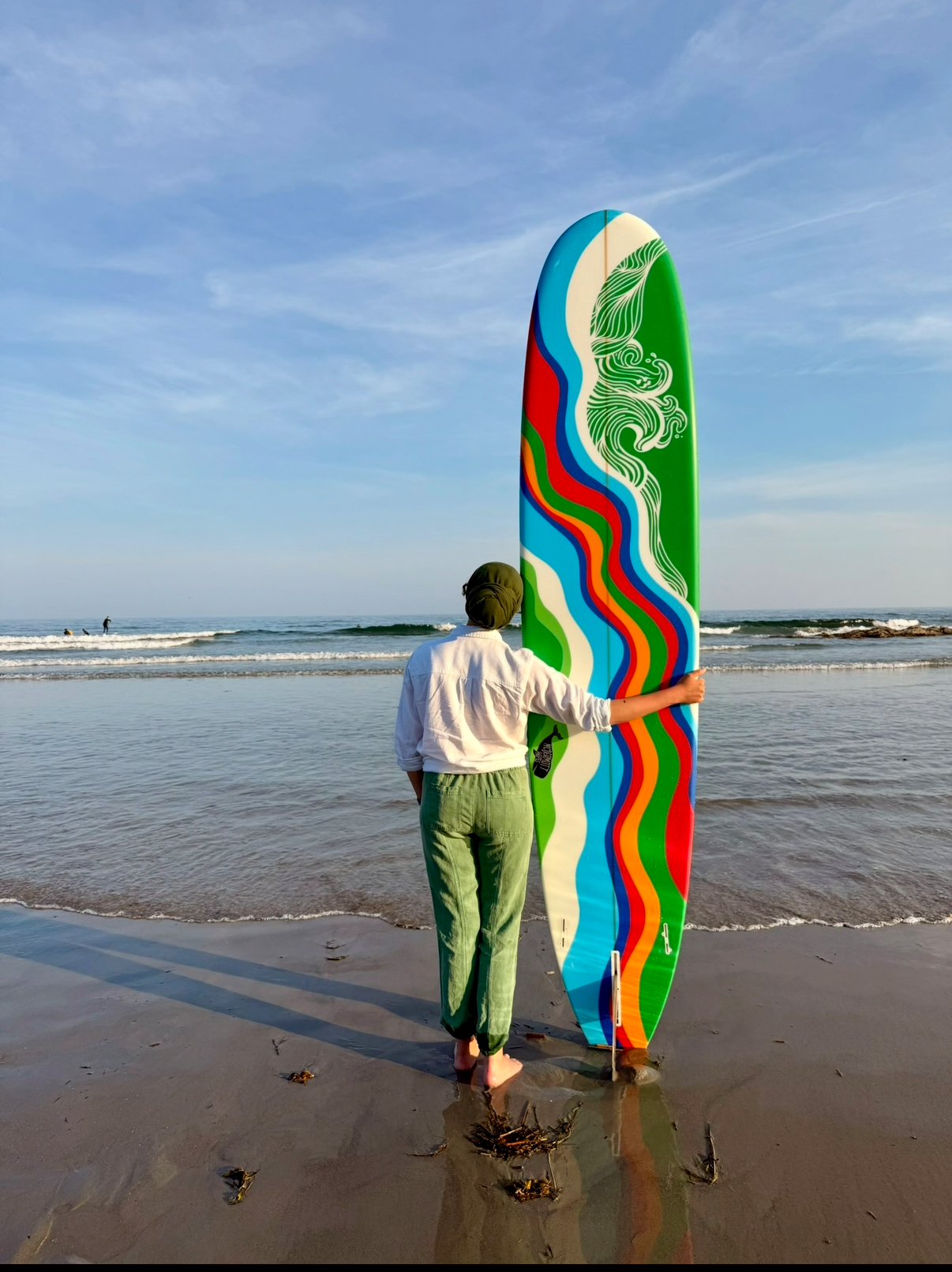 Painted longboard held upright on the beach