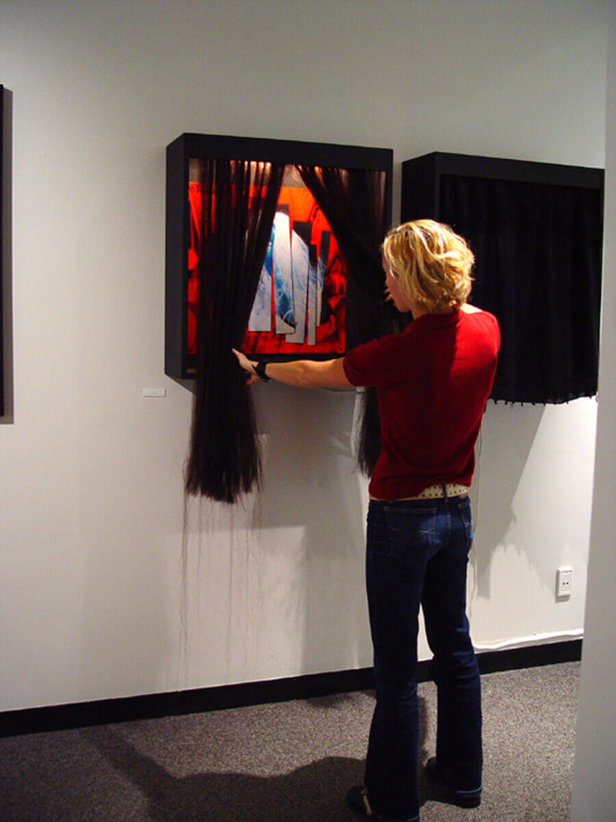Visitor parting a hair curtain over a framed work